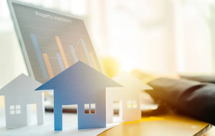 Paper cutout houses in front of a “Property Investment” bar chart, symbolizing marketing and sale of an outdoor resort lot.