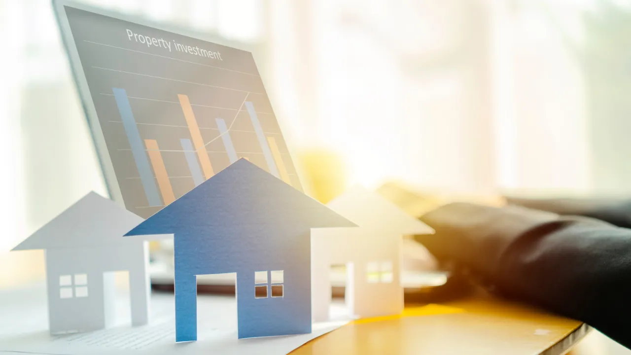 Paper cutout houses in front of a “Property Investment” bar chart, symbolizing marketing and sale of an outdoor resort lot.