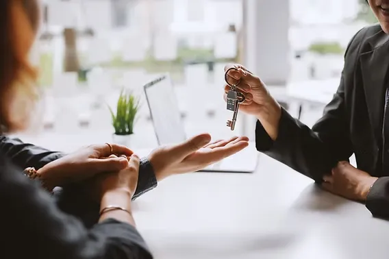 Real estate agent handing keys to a client across a desk, representing closing a sale on an RV lot or resort property.